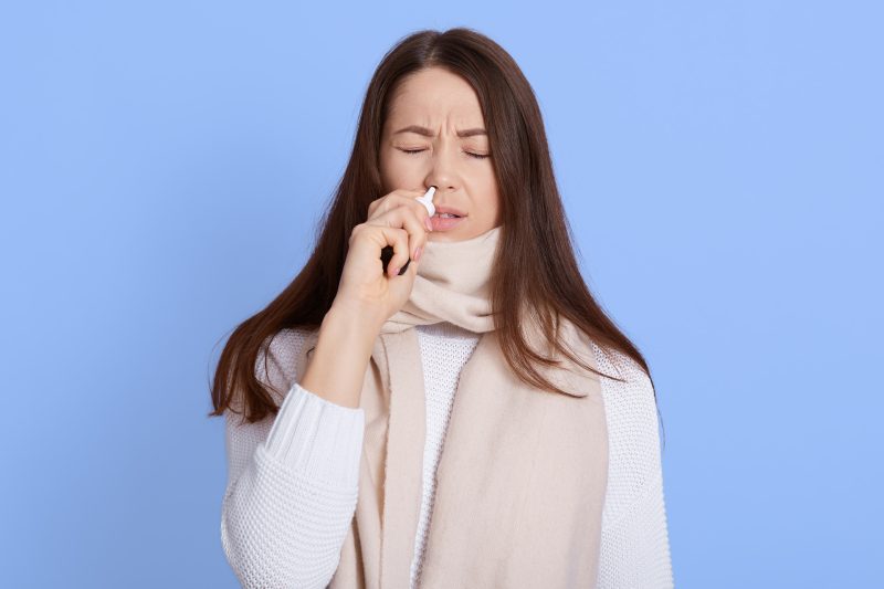 Woman using nasal spray to reduce Long Covid symptoms